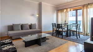 Una sala de estar moderna con un sofá gris, una mesa de centro de vidrio y un comedor con mesa y sillas de vidrio.