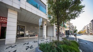 Un edificio moderno con fachada de tejas, una entrada visible y un árbol en primer plano.