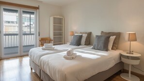 Une chambre d’hôtel avec un grand lit, une table de chevet avec une lampe, une chaise en bois et une porte-fenêtre coulissante donnant sur le balcon.