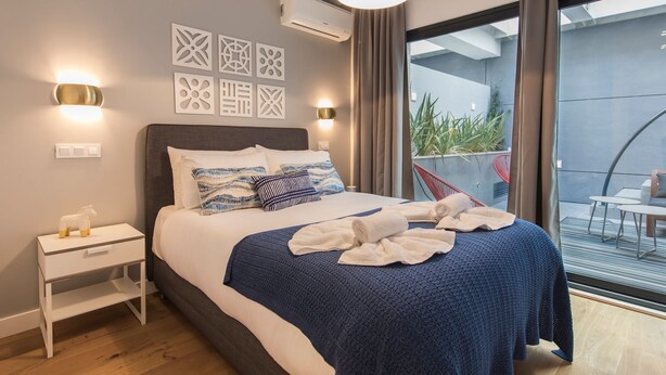 Une chambre d’hôtel moderne dotée d’un grand lit, d’une table de chevet, d’un climatiseur fixé au mur et offrant une vue sur le balcon extérieur.