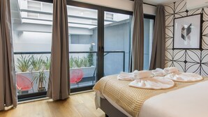 Une chambre d’hôtel avec un lit, un balcon agrémenté de plantes et un fauteuil rouge.
