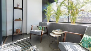 A modern living room with a grey sofa, a wooden chair, a small round table, and a bookshelf.
