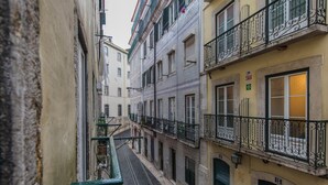 A narrow street with buildings on both sides, featuring balconies with wrought iron railings and a visible fire alarm sign.