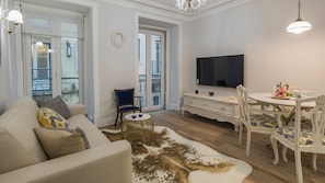 A living room with a sofa, a coffee table, a dining table with chairs, a TV, and a view of the outside balcony.