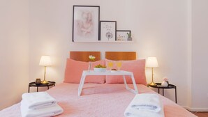 A neatly made bed with pink bedding, two bedside lamps, a tray with a flower and glasses of orange juice, and a framed picture above the bed. - Charming Chiado 2BDR W/Balcony by LovelyStay (Encarnação)