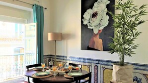 A dining area with a table set for breakfast, a potted plant, and a painting of a flower on the wall. - Charming Chiado 2BDR W/Balcony by LovelyStay (Encarnação)