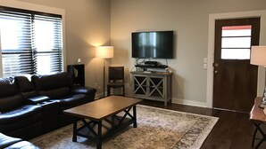 A living room with a leather couch, a coffee table, a TV on a stand, a lamp, and a door.