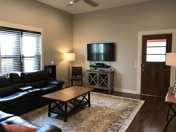 A living room with a leather couch, a coffee table, a TV on a stand, a lamp, and a door.