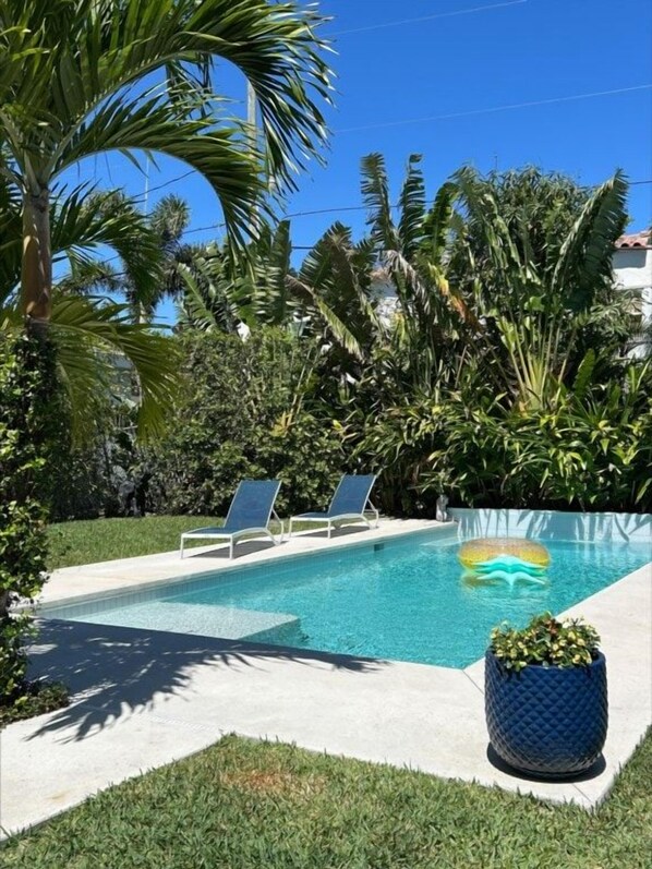 Una piscina con sillas de descanso y plantas tropicales.