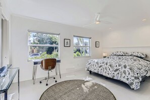 Ein Schlafzimmer mit einem Bett, einem Schreibtisch, einem Stuhl und zwei Fenstern.