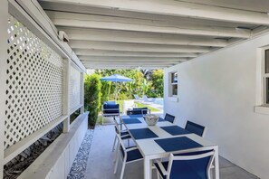 Eine Terrasse im Freien mit einem weißen Tisch und Stühlen, einem blauen Sonnenschirm und einem weißen Zaun.