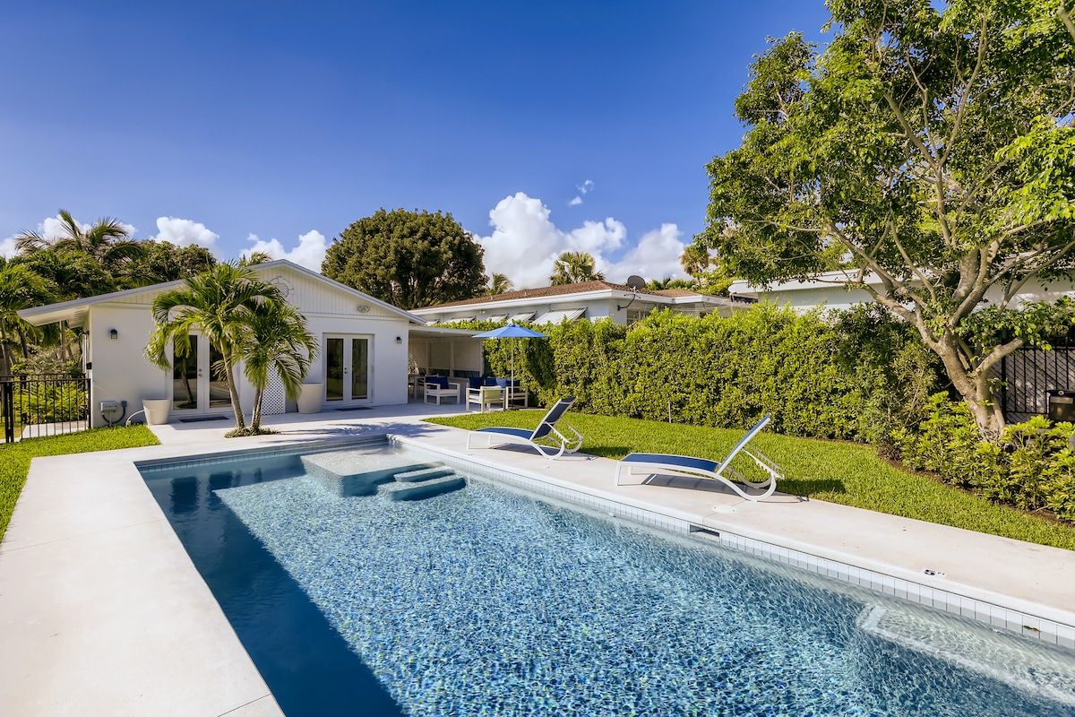 A swimming pool with lounge chairs, a small building, and a well-maintained garden.