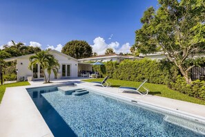 Une piscine avec des chaises longues, un petit bâtiment et un jardin bien entretenu.