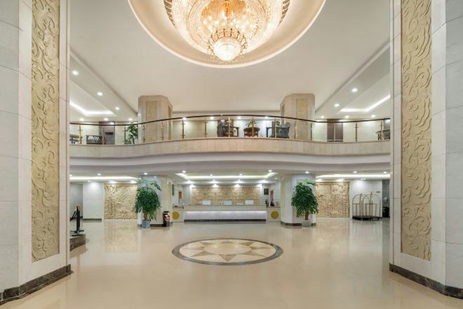 A spacious lobby with a grand chandelier, a reception desk, and a circular floor design.