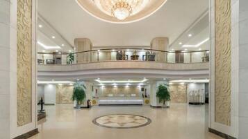 A spacious lobby with a grand chandelier, a reception desk, and a circular floor design.