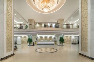 A spacious lobby with a grand chandelier, a reception desk, and a circular floor design.