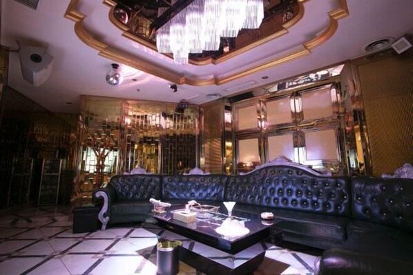 A luxurious interior with a black leather sofa, a glass coffee table, and ornate gold detailing on the walls and ceiling.