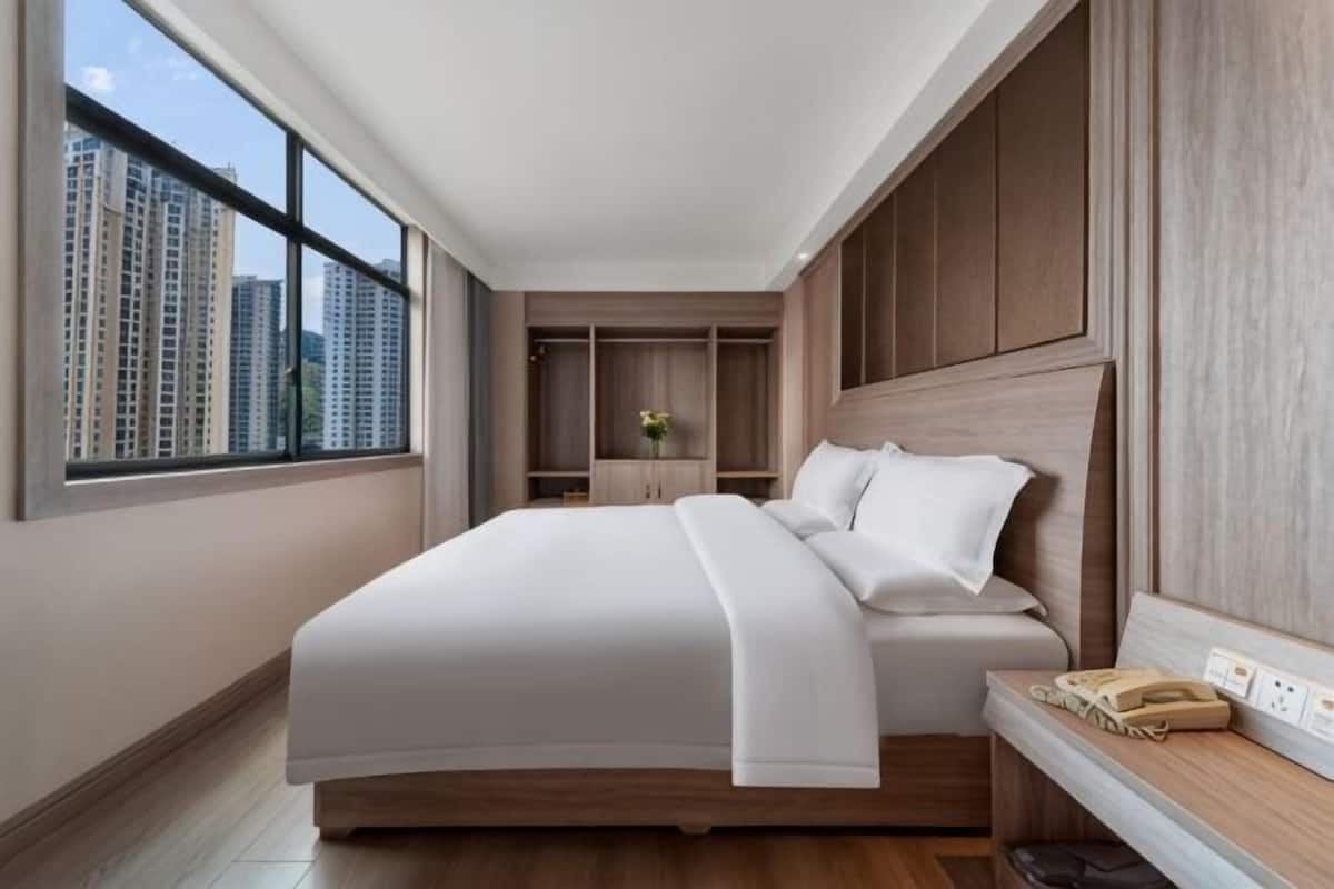 Une chambre d’hôtel moderne dotée d’un grand lit, d’une armoire intégrée et offrant une vue sur de hauts immeubles.