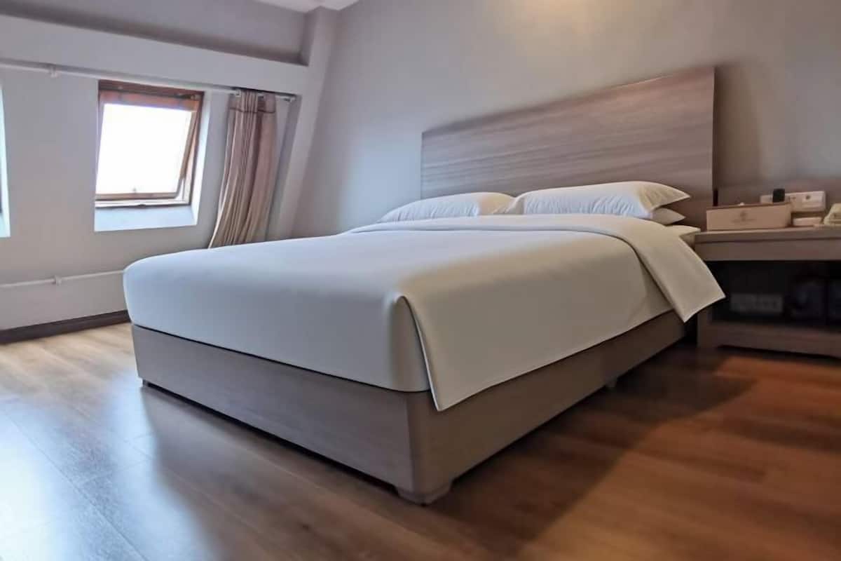 Une chambre d’hôtel moderne avec un grand lit, une table de chevet, une commode et une fenêtre avec des rideaux.