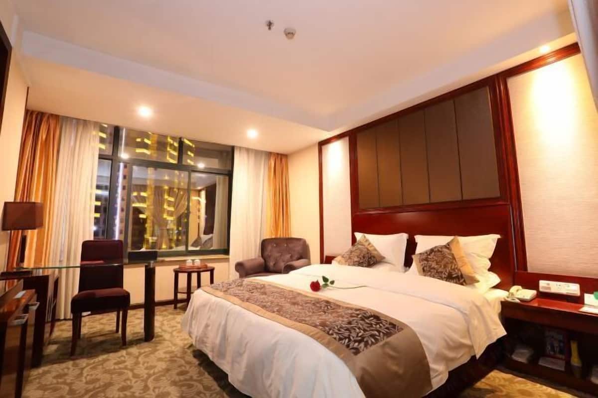 Une chambre d’hôtel avec un grand lit, un bureau avec une chaise, une petite table et une fenêtre avec des rideaux.