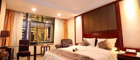 A hotel room with a large bed, a desk with a chair, a small table, and a window with curtains.