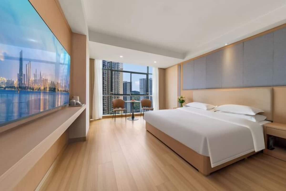 Une chambre d’hôtel moderne avec un grand lit, une vue sur le paysage urbain, une petite table avec des chaises et une grande fenêtre.
