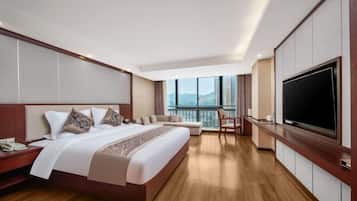 A modern hotel room with a large bed, a TV, a balcony with a city view, and a wooden floor.