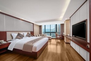 A modern hotel room with a large bed, a TV, a balcony with a city view, and a wooden floor.