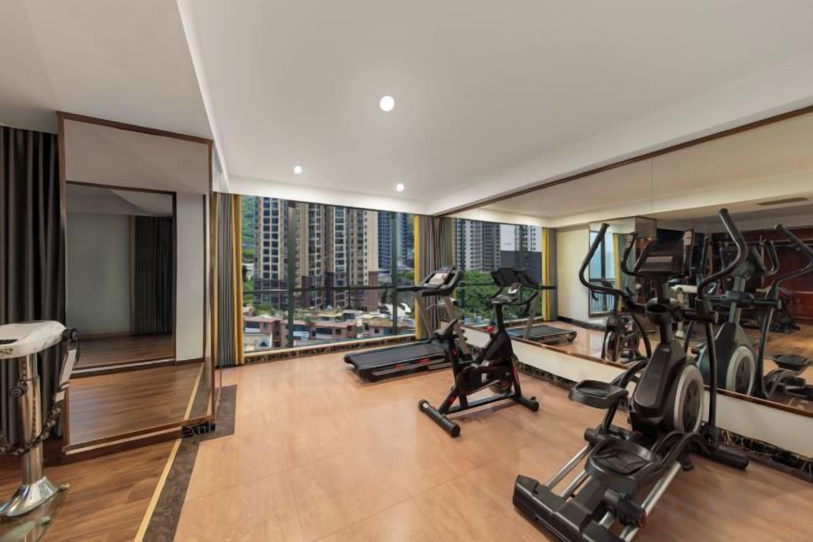 A spacious gym with cardio machines, a mirror, and a view of high-rise buildings.