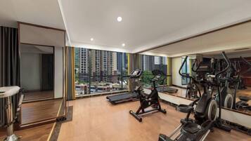 A spacious gym with cardio machines, a mirror, and a view of high-rise buildings.