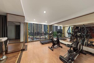 Un gimnasio amplio con máquinas de cardio, un espejo y vistas a rascacielos.