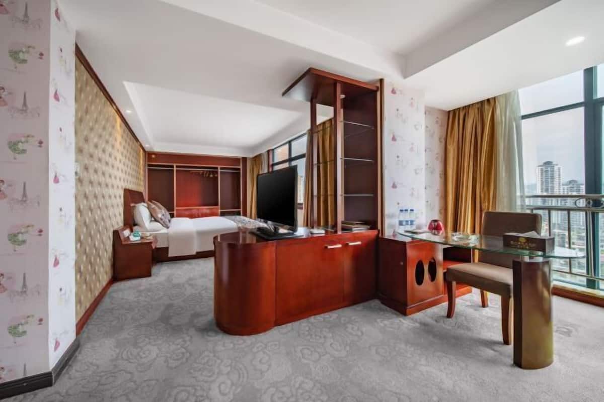 Une chambre d’hôtel comprenant un lit, une télévision, un bureau avec une chaise, une armoire et une grande fenêtre donnant sur la ville.