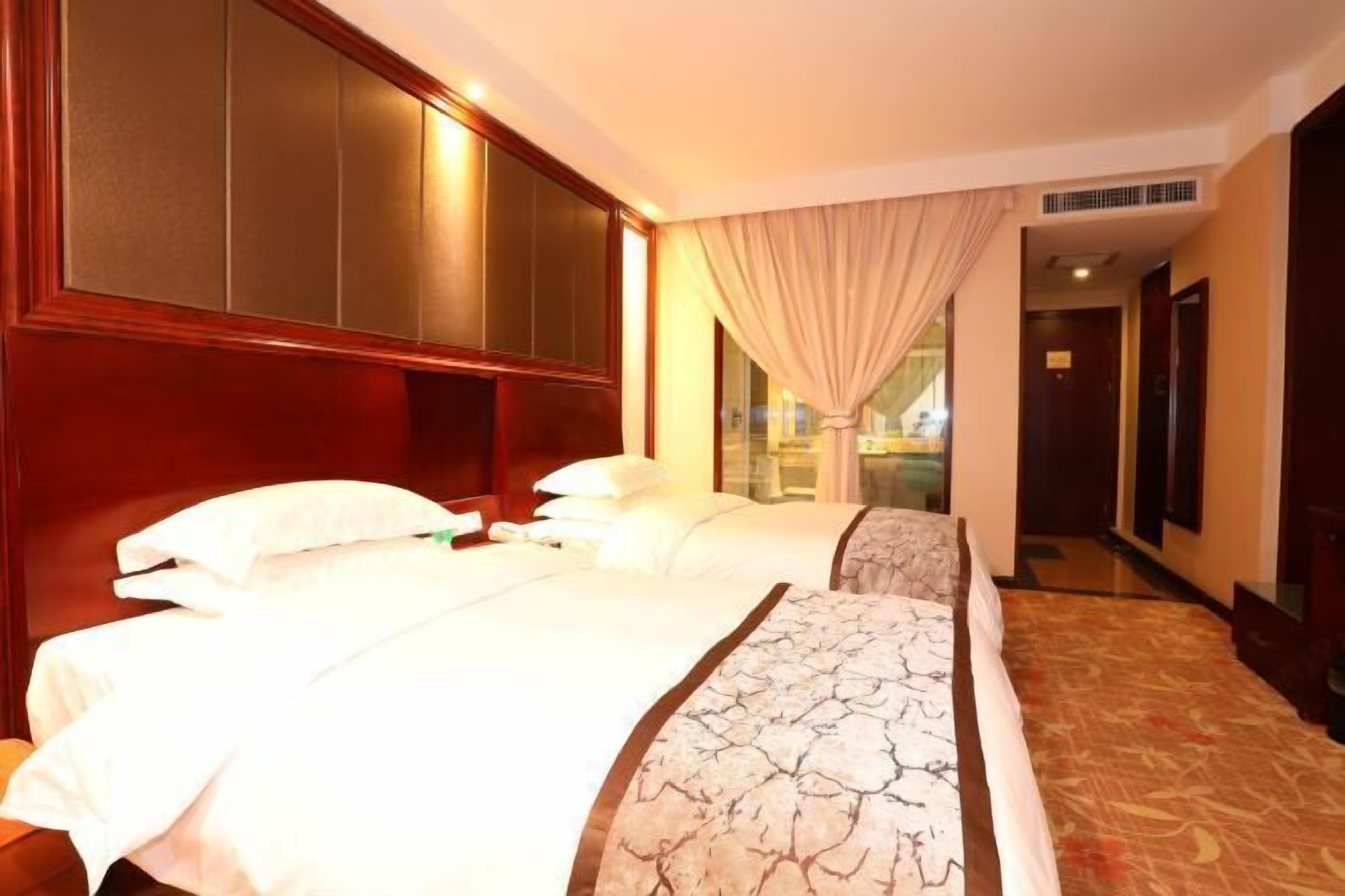 Habitación de hotel con dos camas, un ventanal con cortinas y suelo alfombrado.