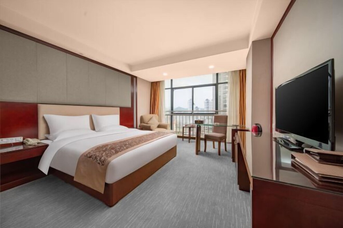 A hotel room with a large bed, a TV, a desk, and a chair.