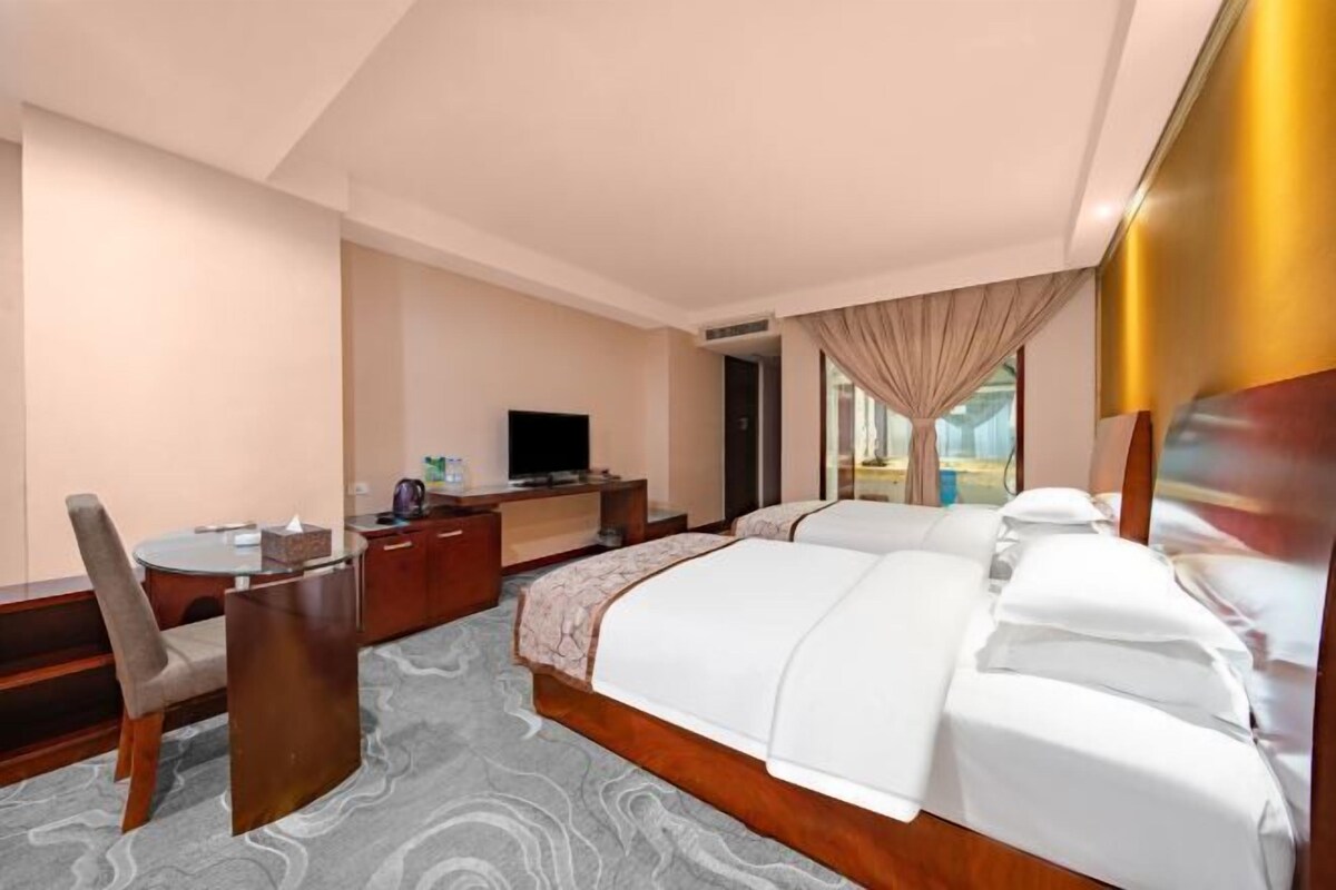 A hotel room with a bed, a desk, a chair, a television, and a window with curtains.