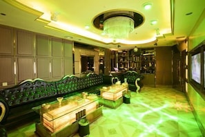 Een luxueus loungegedeelte met een vloer in groene verlichting, een comfortabele groene bank en een kroonluchter.