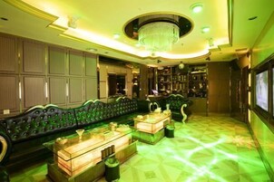 A luxurious lounge area with a green-lit floor, a plush green sofa, and a chandelier.