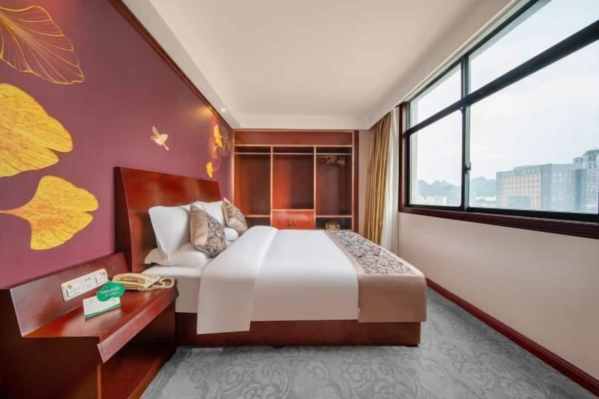Une chambre d’hôtel avec un grand lit, une table de chevet, une armoire et une fenêtre donnant sur la ville.