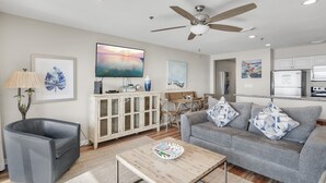 A modern living room with a grey sofa, a wooden coffee table, and a ceiling fan. - Windancer 211. Gulf Front, Free Beach Service, Emerald Waters, Pool, Grill. (Miramar Beach)