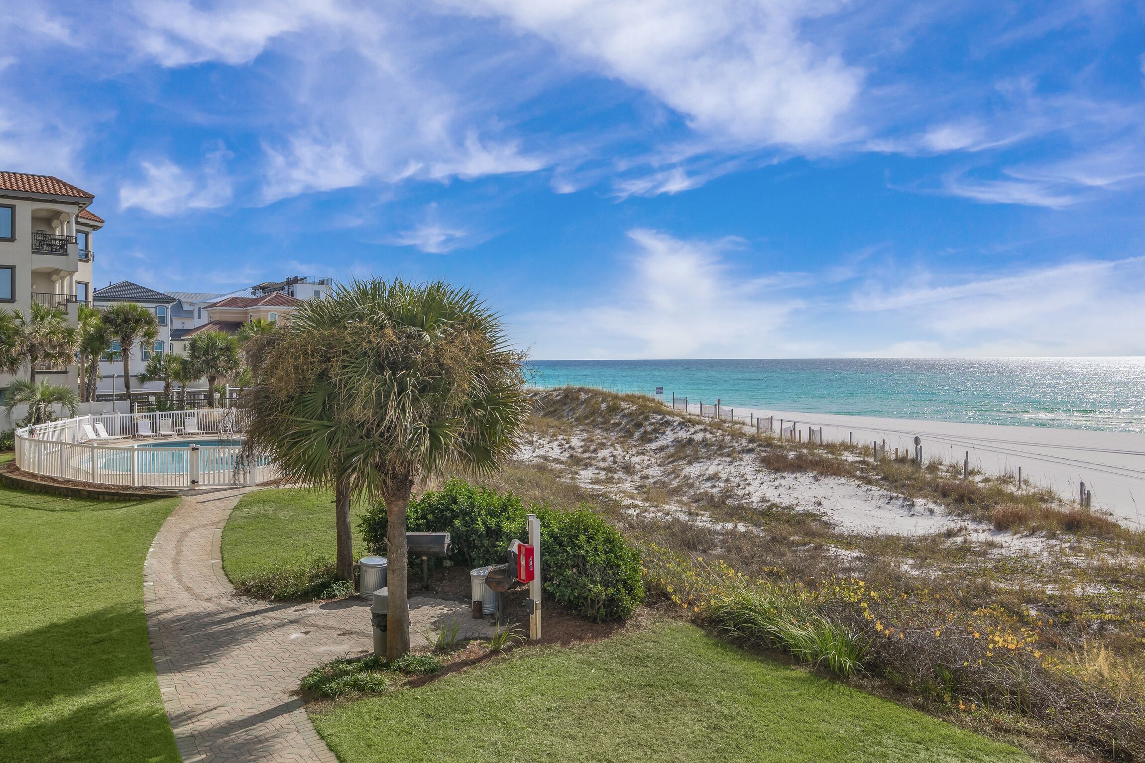 A beachfront property with a swimming pool, a pathway leading to the beach, and a view of the ocean.