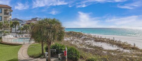 A beachfront property with a swimming pool, a pathway leading to the beach, and a view of the ocean.
