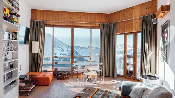 Un salon spacieux doté d’une grande fenêtre offrant une vue sur les montagnes, d’un coin salon confortable et d’une bibliothèque remplie de livres et de jeux.