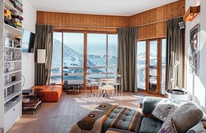 A spacious living room with a large window offering a mountain view, a cozy seating area, and a bookshelf filled with books and games. - Immodreams - Le Renard - Avoriaz (Avoriaz)