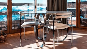 Une pièce dotée d’un plancher en bois, d’une table entourée de chaises, de grandes fenêtres et offrant une vue sur des montagnes enneigées.