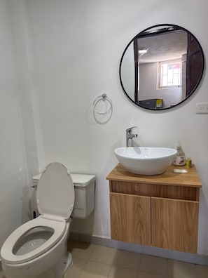 Een badkamer met een toilet, een wastafel met spiegel erboven en een houten kastje eronder.
