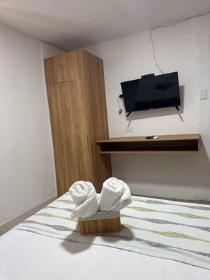 Une chambre à coucher comprenant un lit, une armoire en bois, un téléviseur fixé au mur et un porte-serviettes.