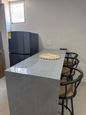 Een keuken met een grijs marmeren aanrecht, een zwarte koelkast en een raam met uitzicht.