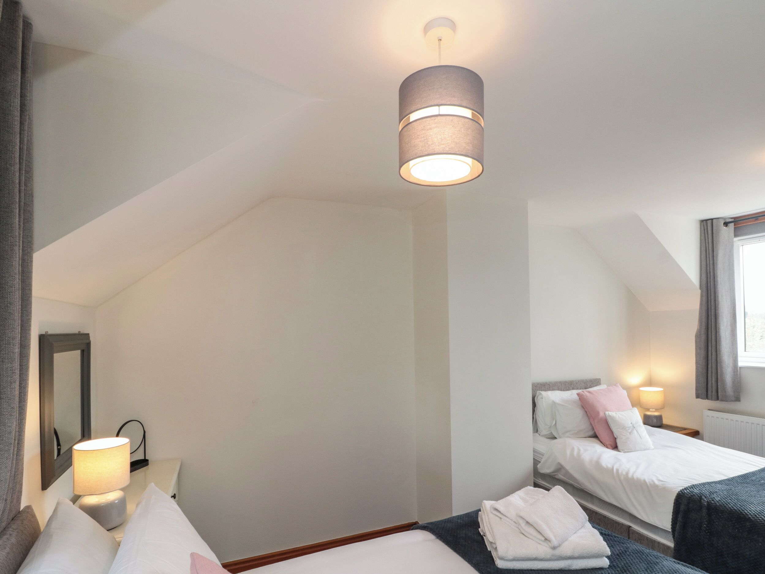 A hotel room with a single bed, a bedside table with a lamp, a mirror, and a window with curtains.