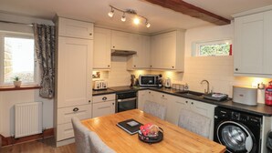 Cocina compacta con armarios blancos, una mesa de comedor de madera, microondas integrado y lavadora.