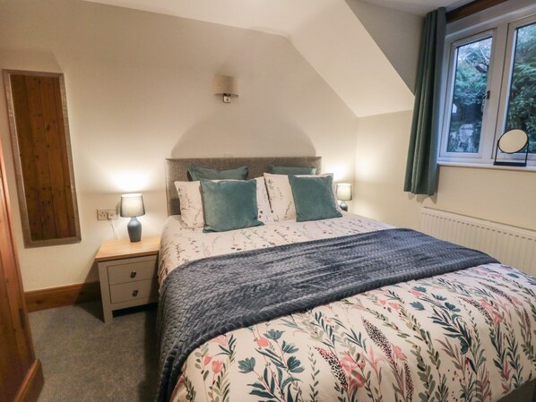 Un dormitorio con cama, mesitas de noche, una ventana con cortinas y una puerta de madera.